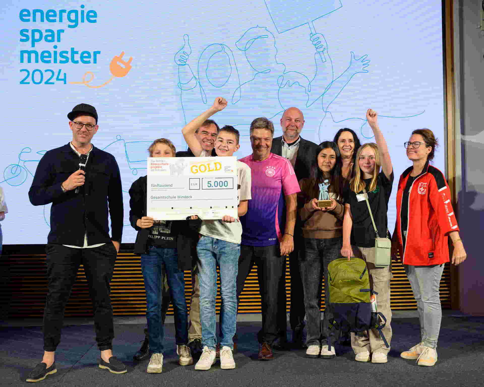 Foto ©co2online / Phil Dera - v. l.: Die Mitglieder der Schülergenossenschaft mit Wirtschaftsminister Robert Habeck im Deutschlandtrikot, daneben Holger Siems und Elisabeth Winkelmeier-Becker, MdB