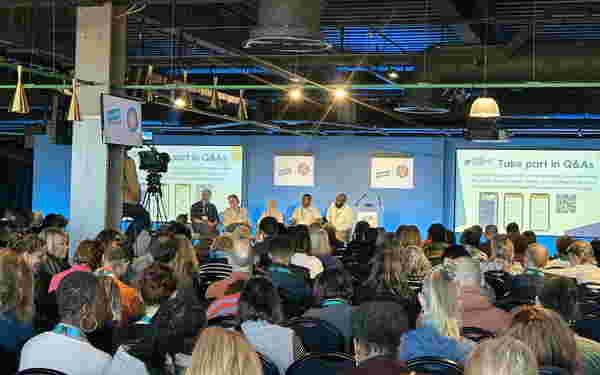 Foto: Viele Menschen sitzen im Publikum. Auf der Bühne eine Diskussionsrunde.